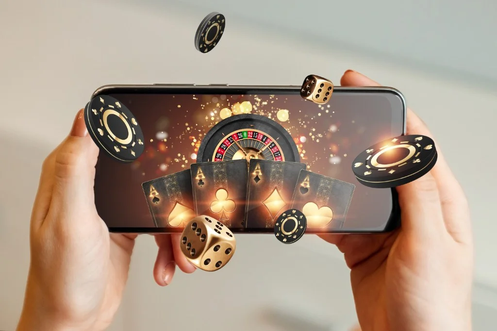 Hands holding a smartphone showing a mobile casino with playing cards, dice, and poker chips — RA88 Malaysia deposits and withdrawals